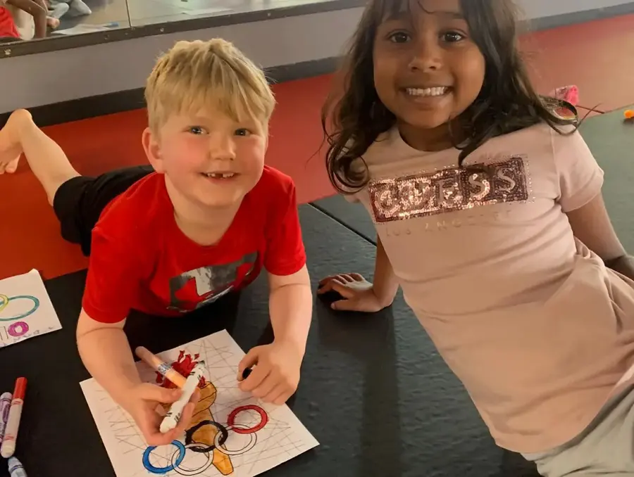 Two children working on a drawing at a table with markers