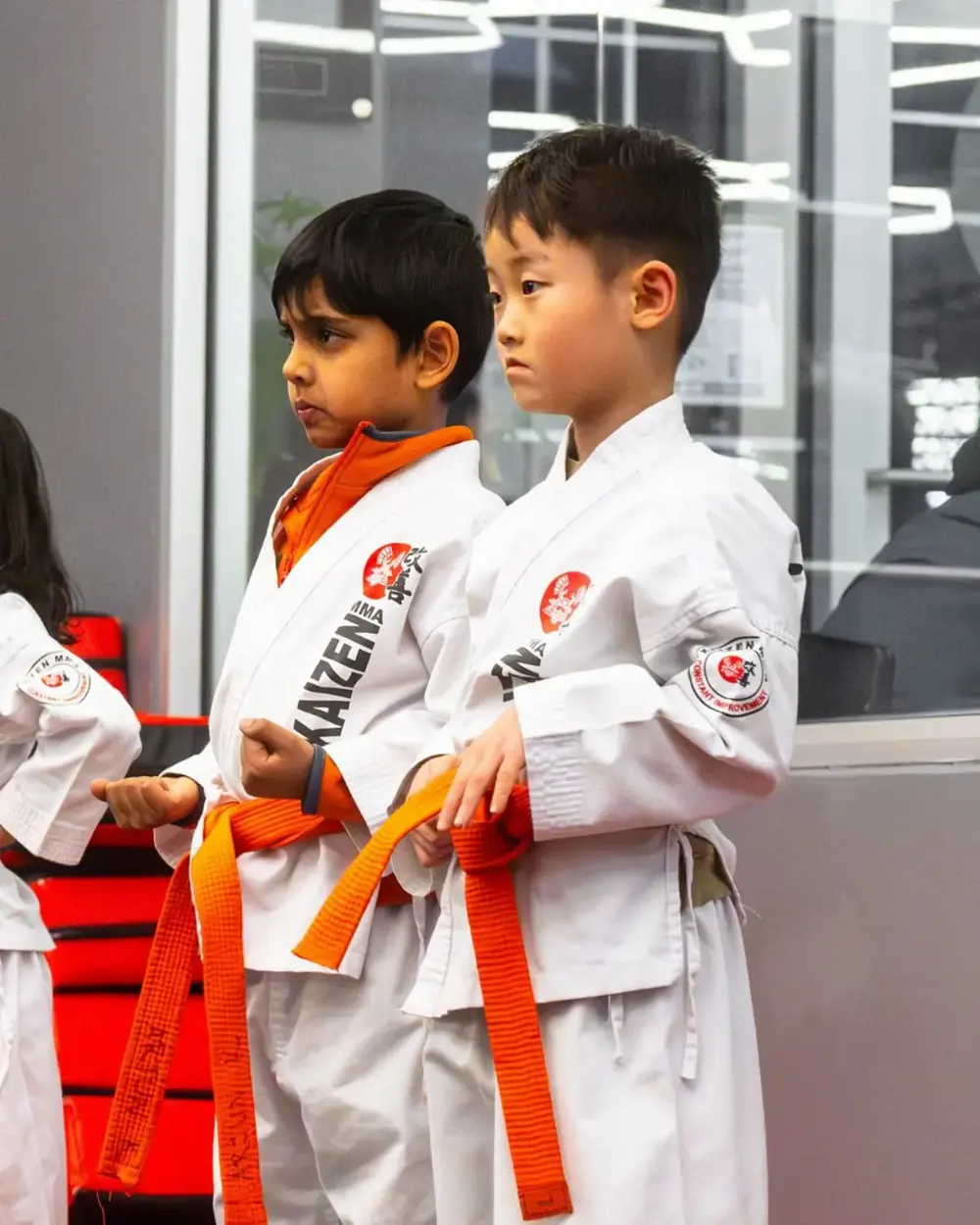Two children standing ready at the edge of the mats before a class