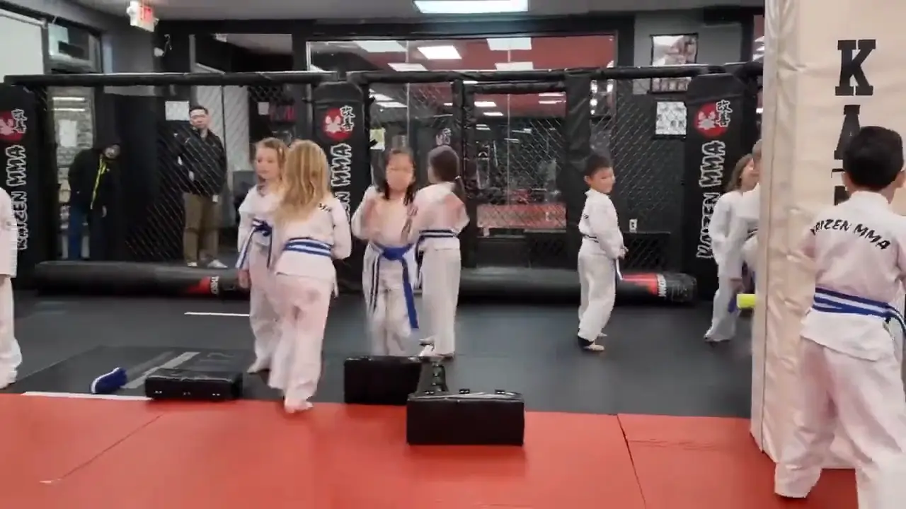 A room of children in white uniforms practicing kicks together on the mats
